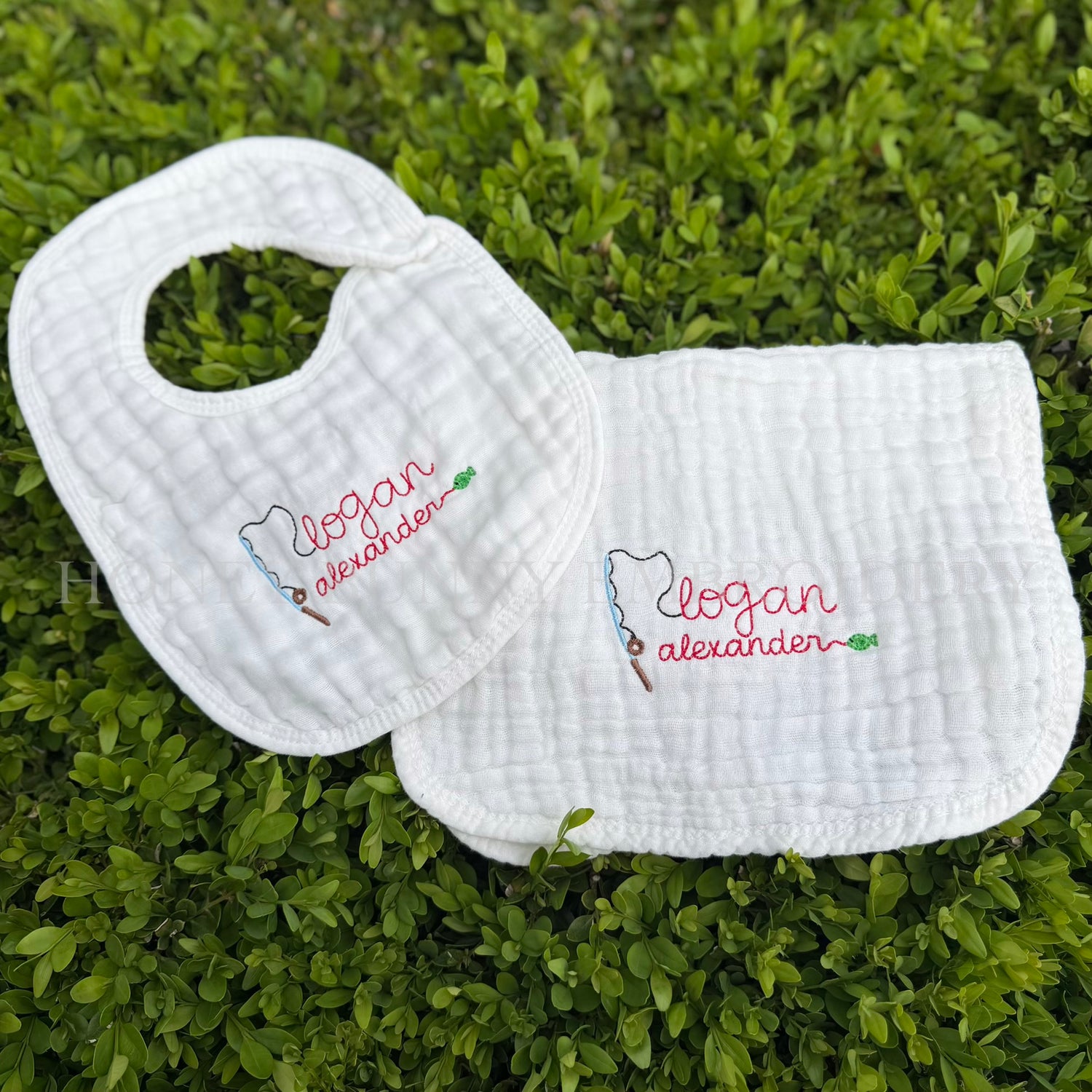 Two white bibs with embroidered names on a grass background