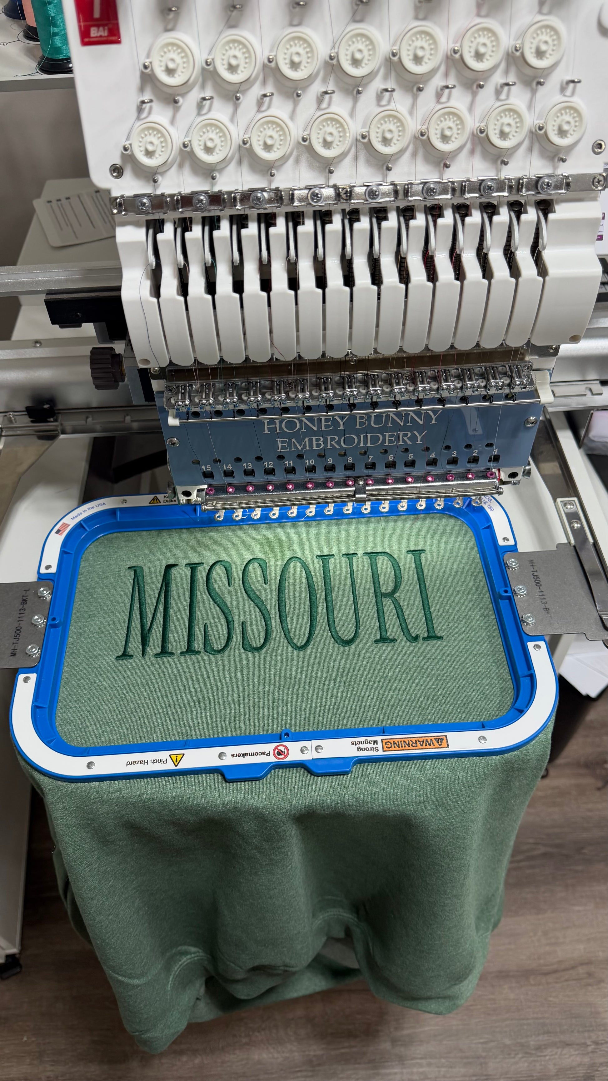 Embroidery machine with a green fabric displaying 'MISSOURI'.