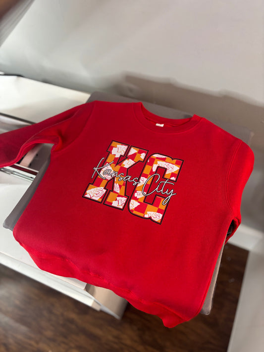 Red sweatshirt with 'Kansas City' design on a white surface