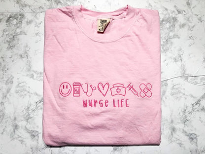 Pink t-shirt with 'NURSE LIFE' text on a marble surface