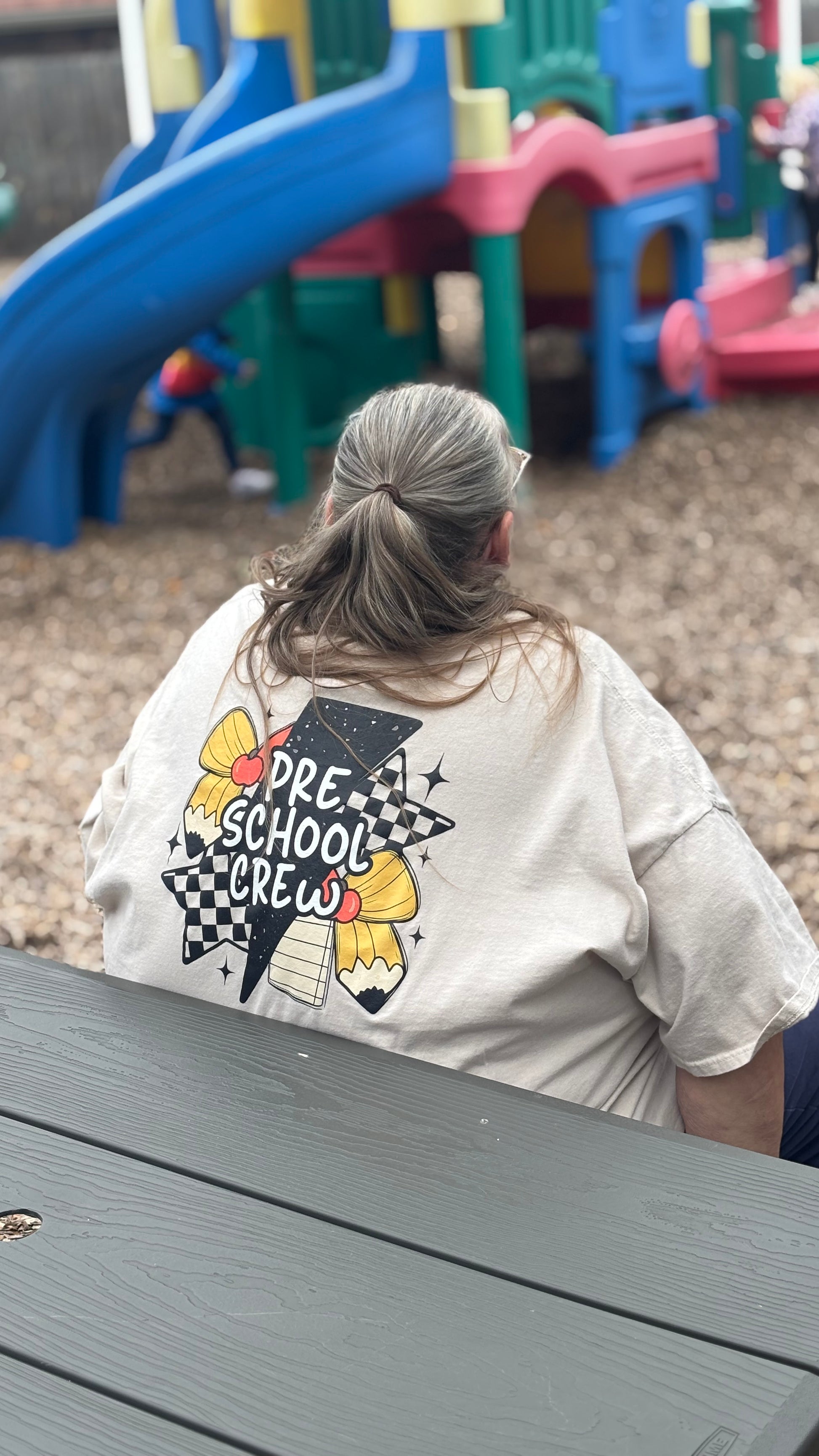Person wearing a shirt with 'Pre-School Crew' design in a playground setting