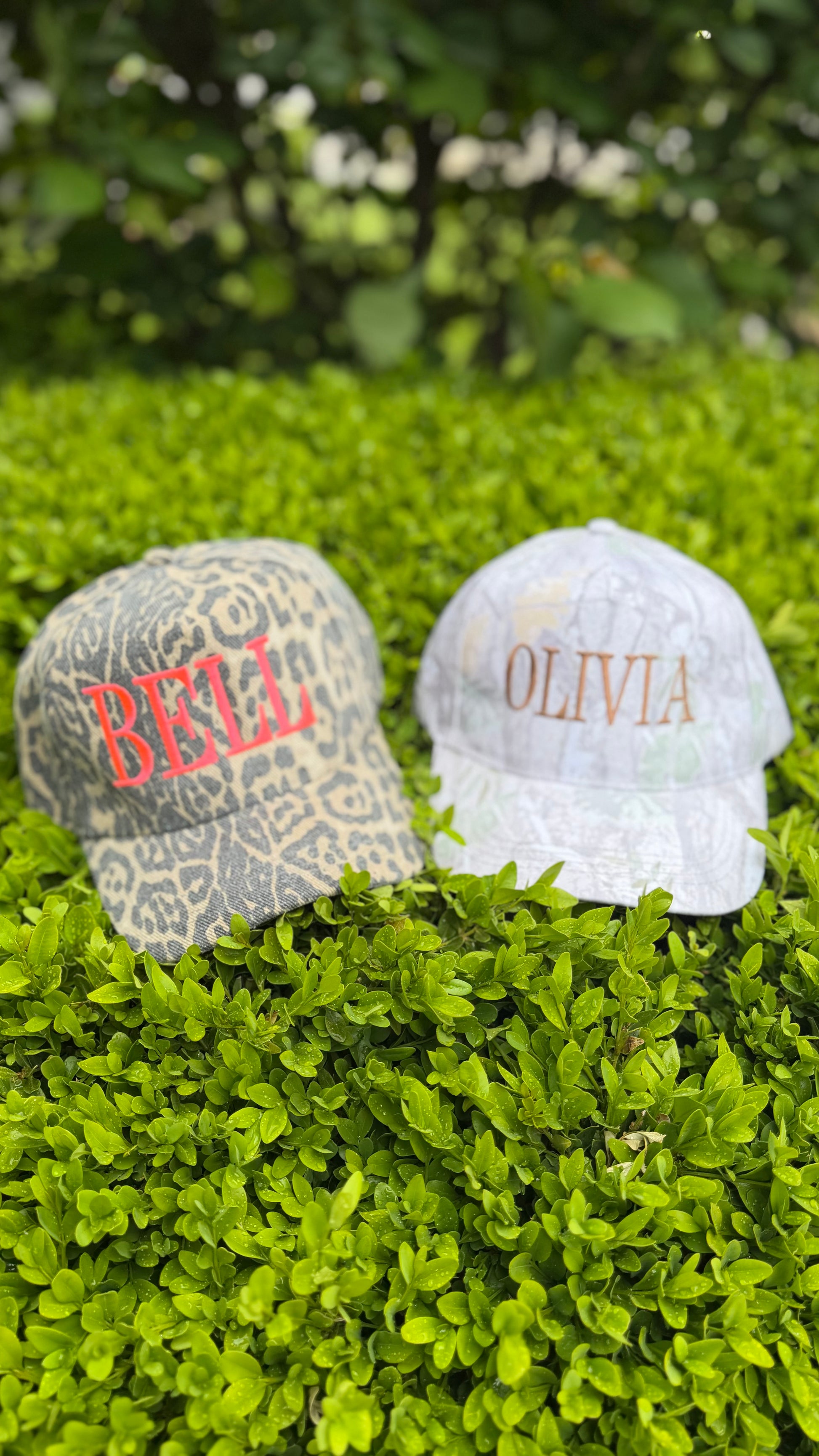 Two baseball caps with embroidered names on a grassy background