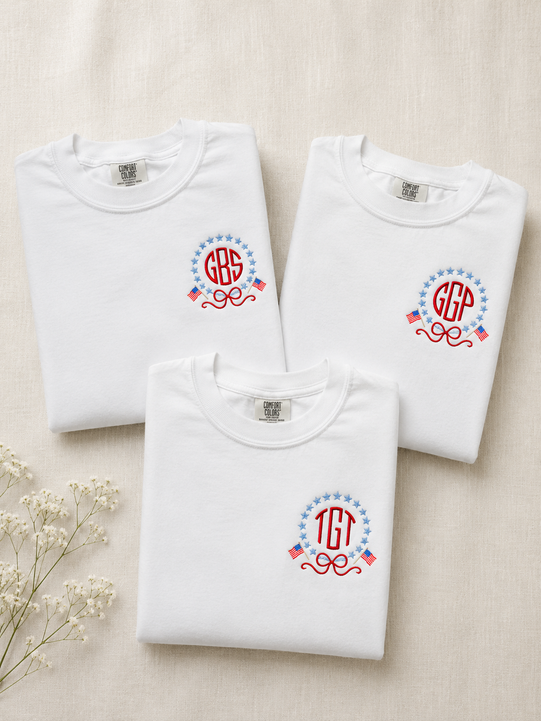 Three folded white sweatshirts with monogram designs on a beige background