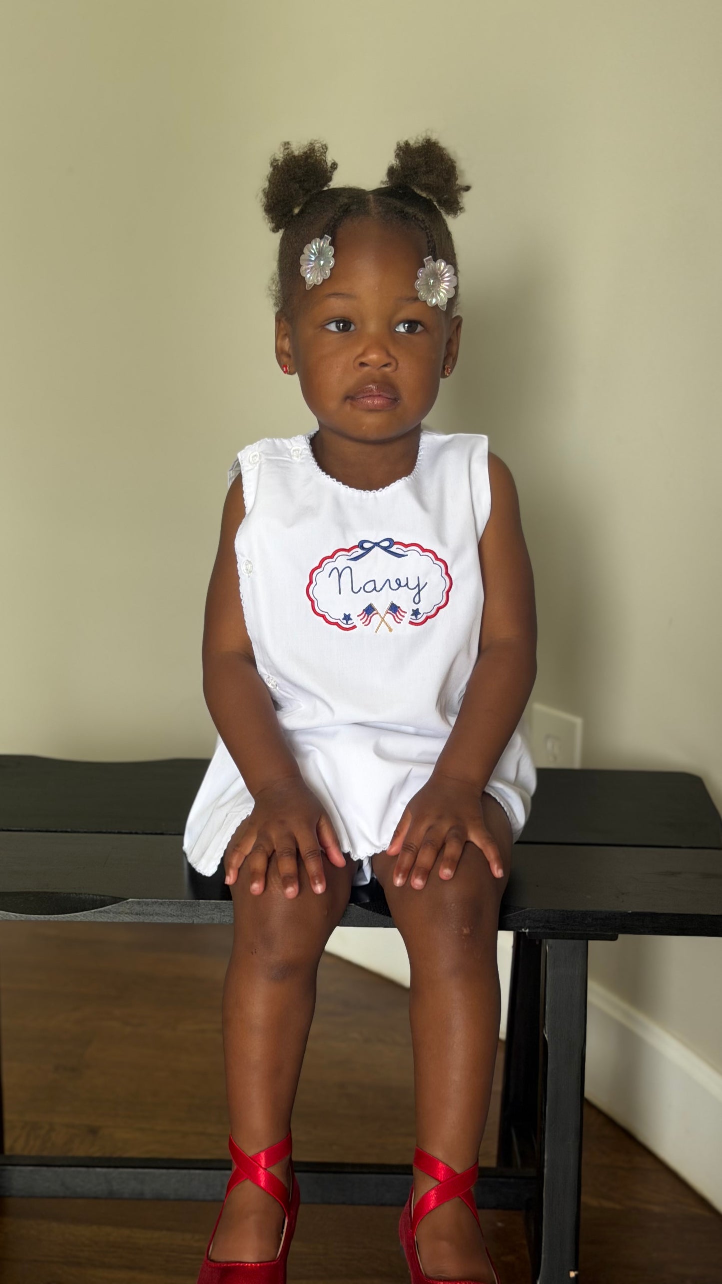 Young girl sitting on a bench wearing a white sleeveless dress with 'Nary' printed on it.