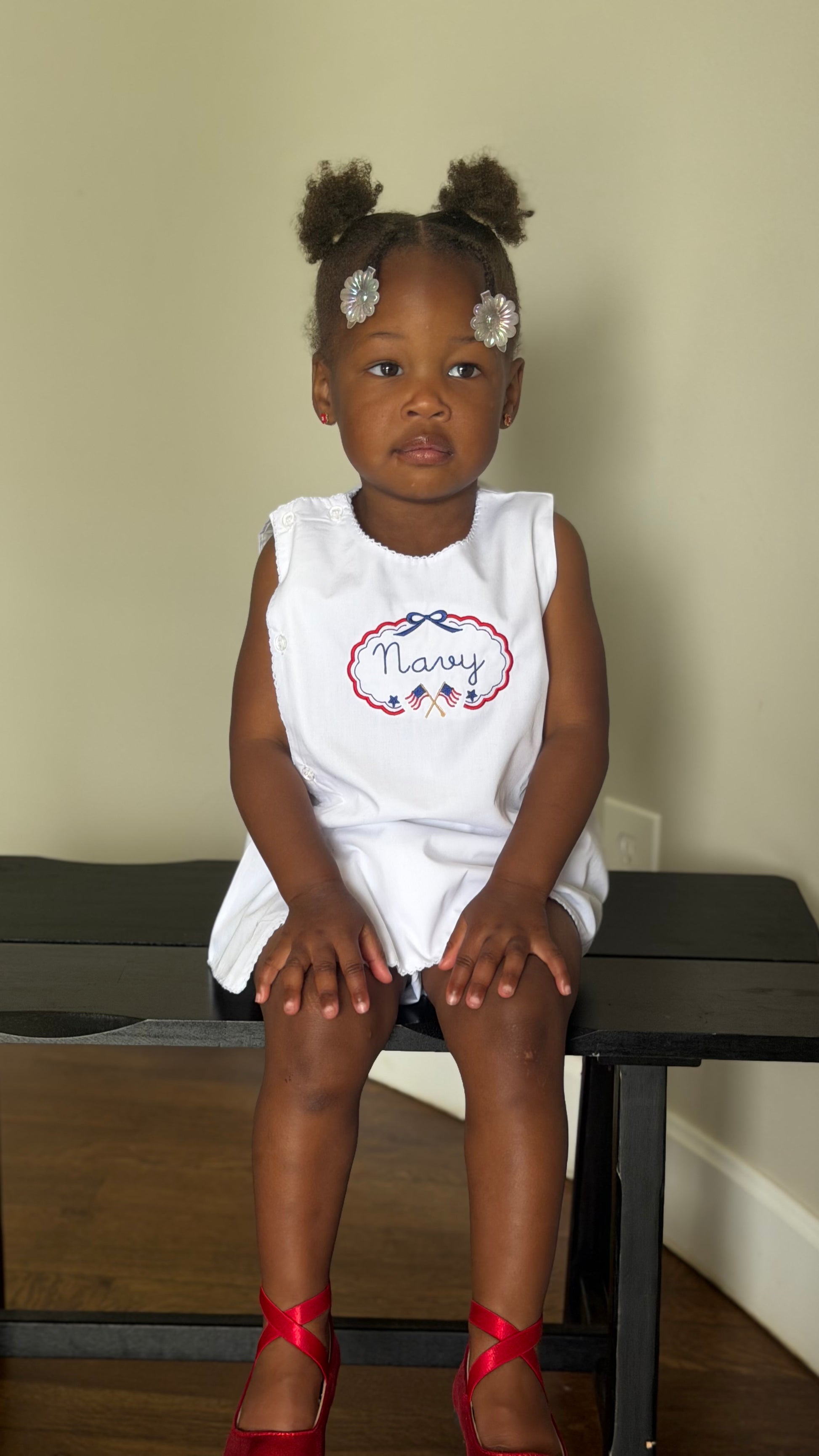 Young girl sitting on a bench wearing a white sleeveless dress with 'Nary' printed on it.