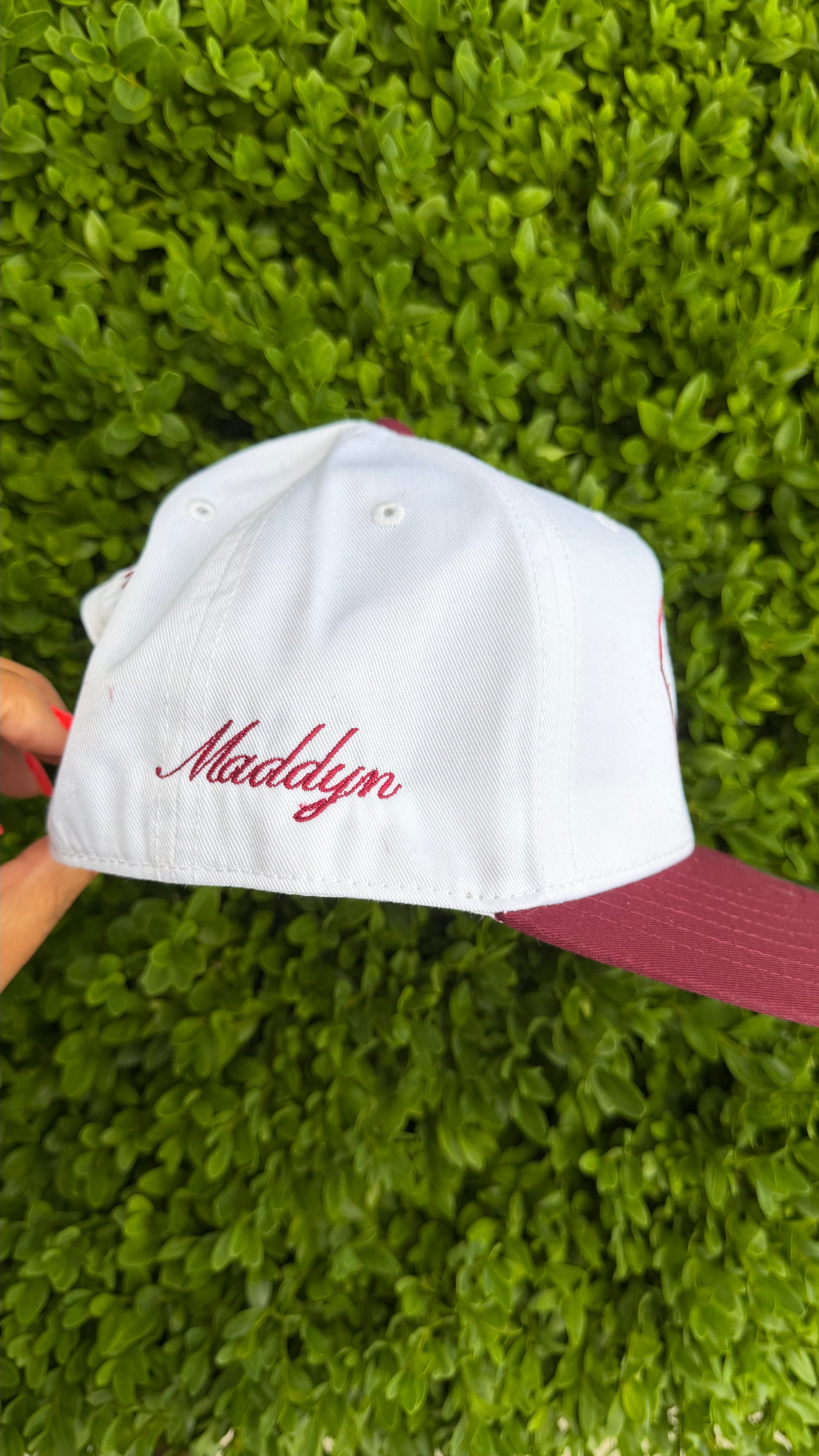 White cap with red text held against a green hedge