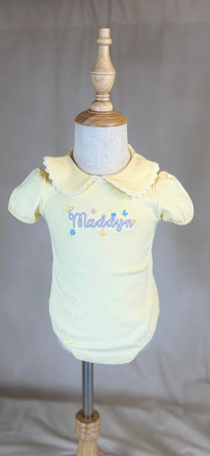 Yellow baby outfit on a mannequin with 'Maddox' embroidered on it against a plain background