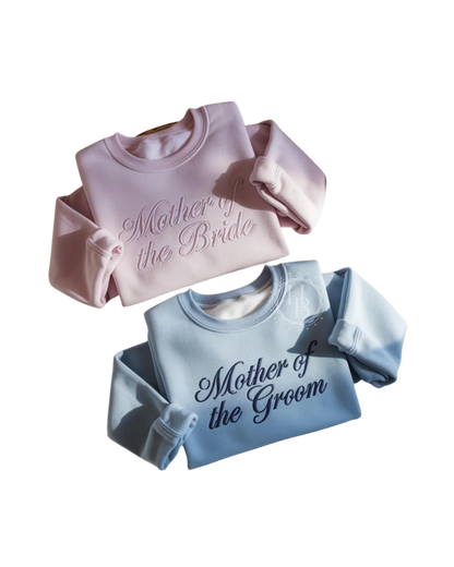 Two sweatshirts, one pink and one blue, with 'Mother of the Bride' and 'Mother of the Groom' text.