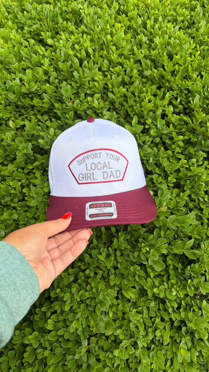 White and maroon cap with text held by a hand against a green grass background