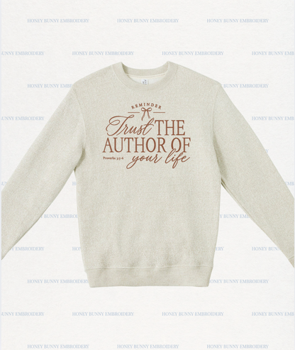 A light beige crewneck sweatshirt with a brown graphic print on the front reading 'Trust THE AUTHOR OF your life' and 'REMINDER' with a small bow illustration. The sweatshirt is displayed flat against a white background with a repeating 'HONEY BUNNY EMBROIDERY' watermark pattern.