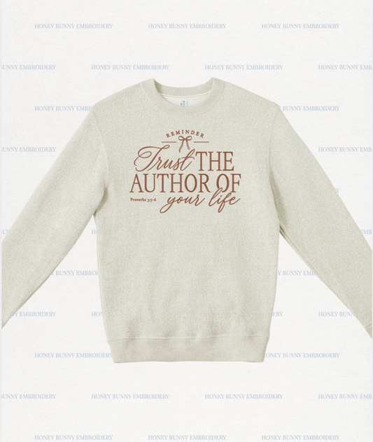 A light beige crewneck sweatshirt with a brown graphic print on the front reading 'Trust THE AUTHOR OF your life' and 'REMINDER' with a small bow illustration. The sweatshirt is displayed flat against a white background with a repeating 'HONEY BUNNY EMBROIDERY' watermark pattern.