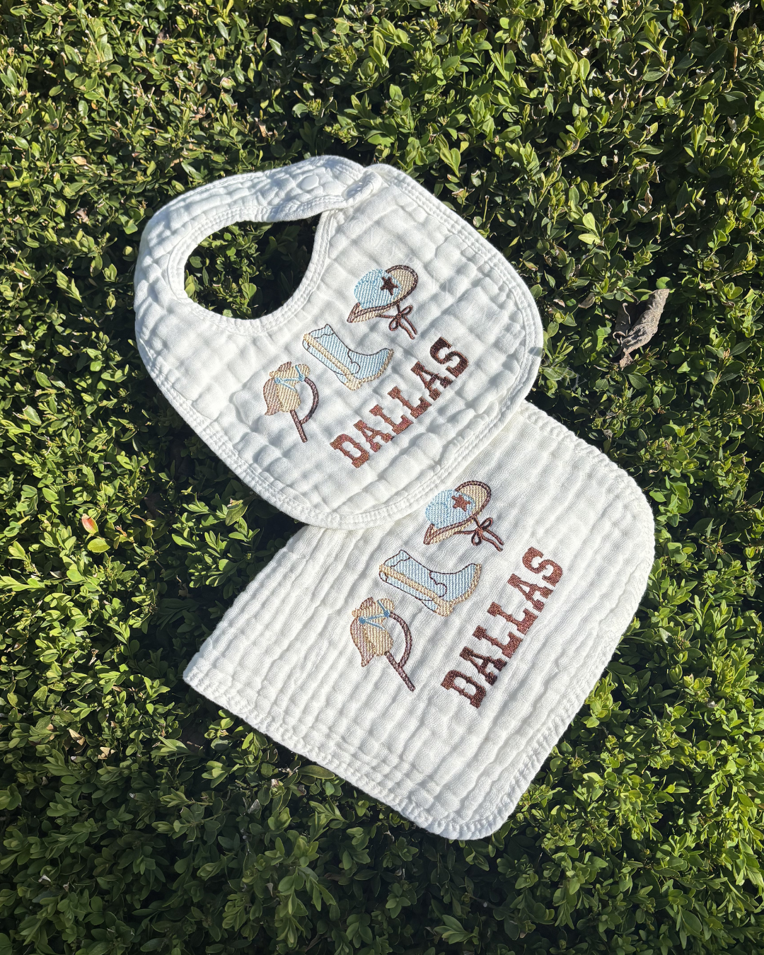 White bib and burp cloth set with 'Dallas' and bull design on grass